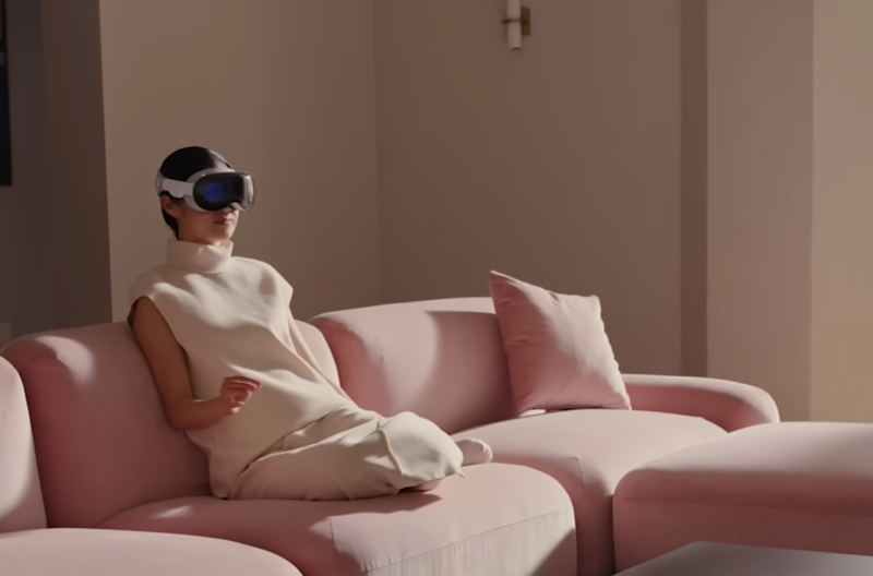 Frau sitzt mit Apple Vision Pro auf dem Sofa und macht kleine Gesten mit der Hand